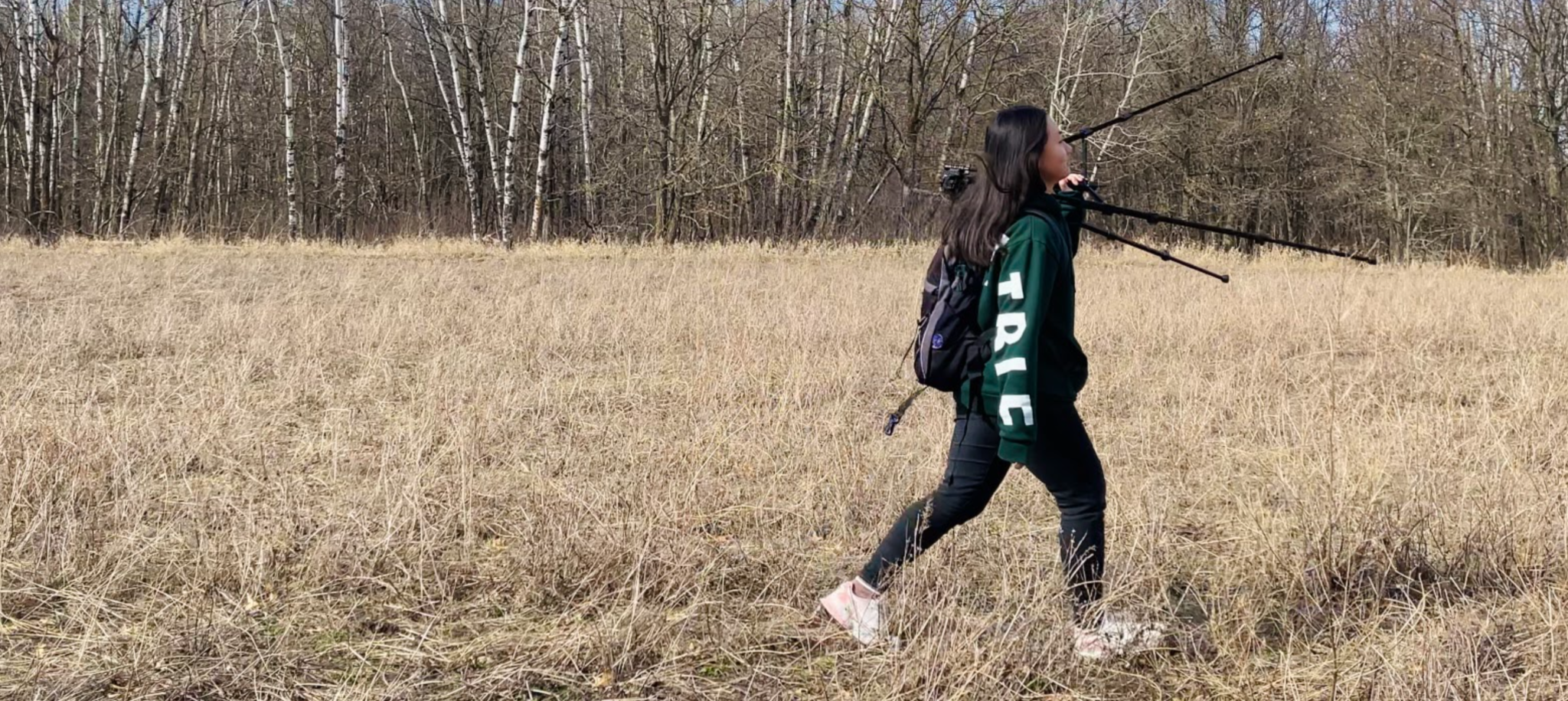 Woman walking with a tripod across a field