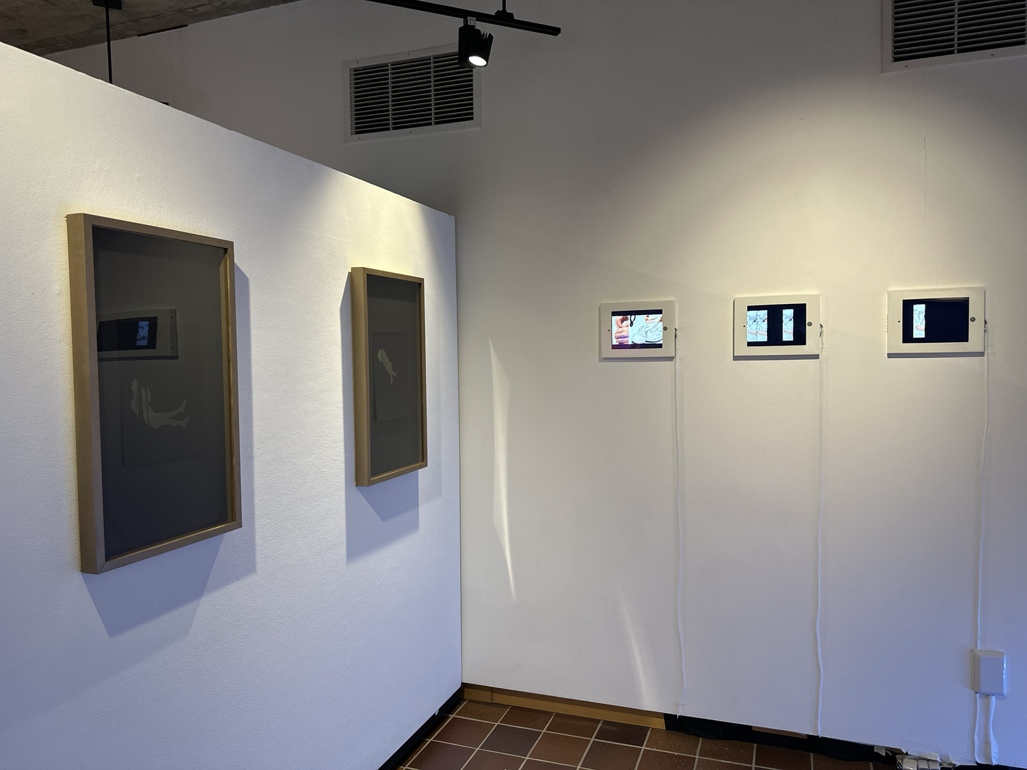Two framed works and three iPads in a row of Ellen Mueller's work. The details of each work are difficult to see from this camera distance.
