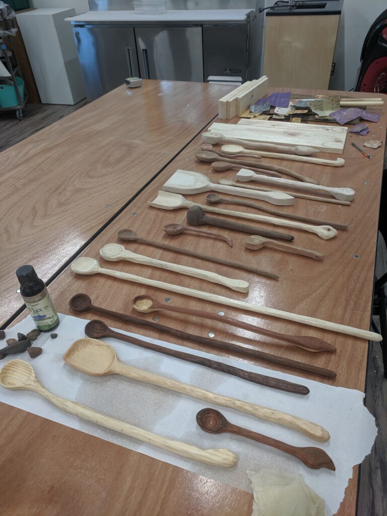Wooden tabletop with many types of whittled wooden spoons resting on it.